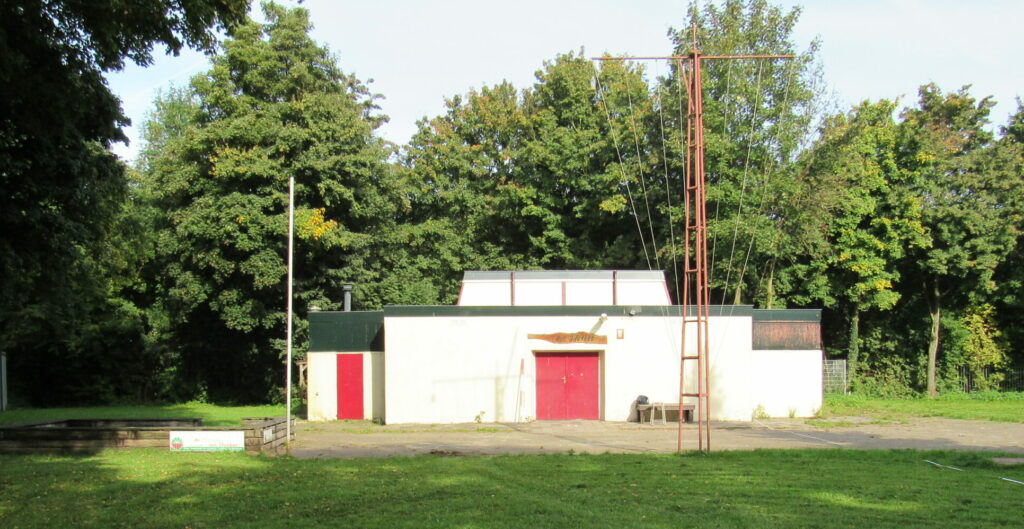 OUDE SITUATIE: oud wit scoutinggebouw, met groene boeiboorden en rode deuren