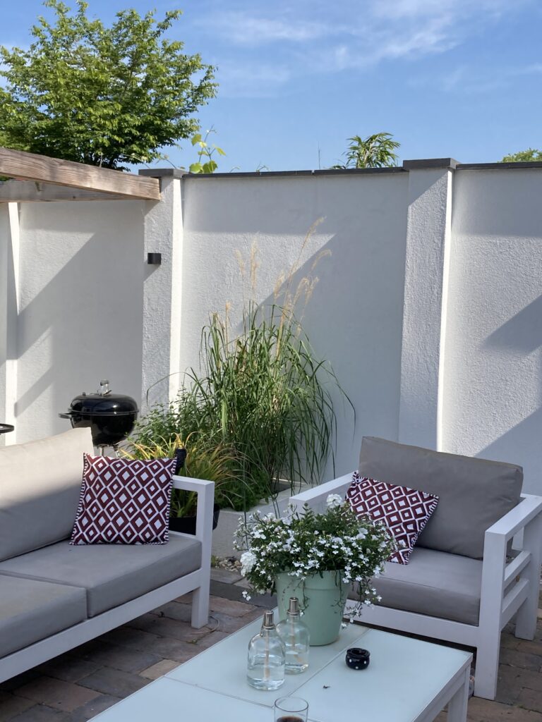 PARTICULIER (3) NIEUW ONTWERP: zalig terras met witte loungeset en kussens met dessin, witte tuinmuren, pergola en siergrassen